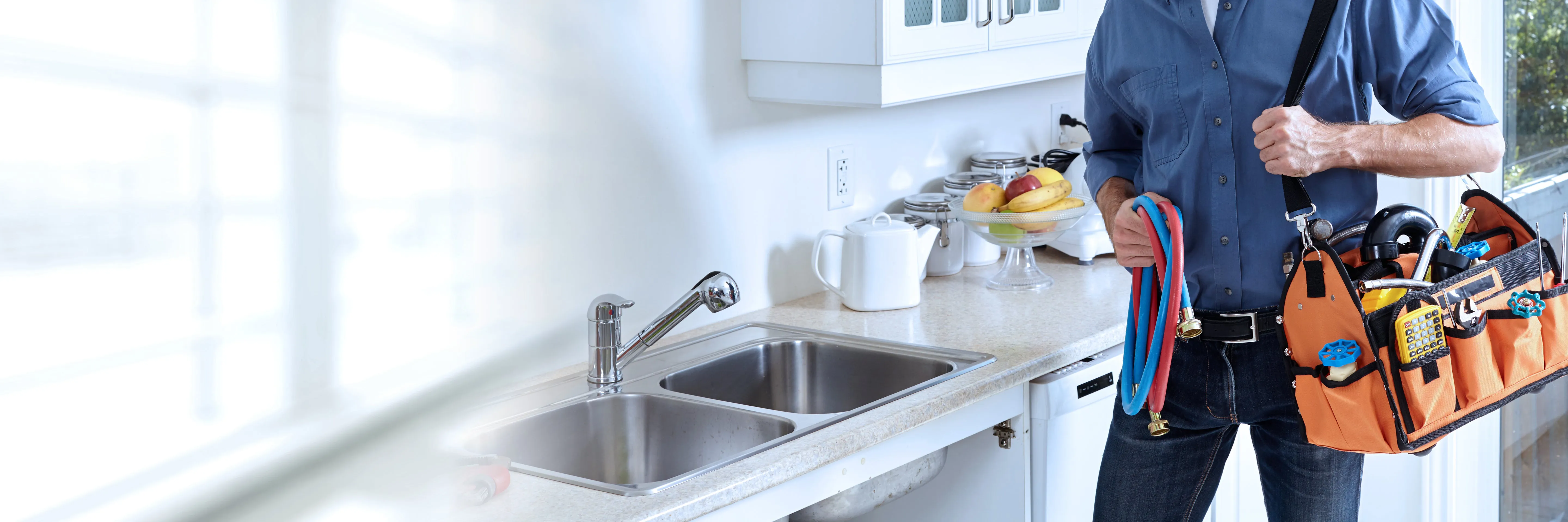"A plumber from Smart Plumbers, Inc. in Santa Clara holding a tool bag in a kitchen with a double sink and a neatly arranged countertop."