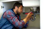 A plumber from Smart Plumbers, Inc. in Santa Clara working under a sink with a wrench.