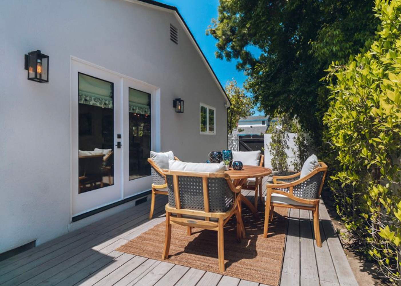 A wooden patio with a round table and four cushioned chairs, surrounded by greenery, constructed by Smith & Son Construction in Martinez.