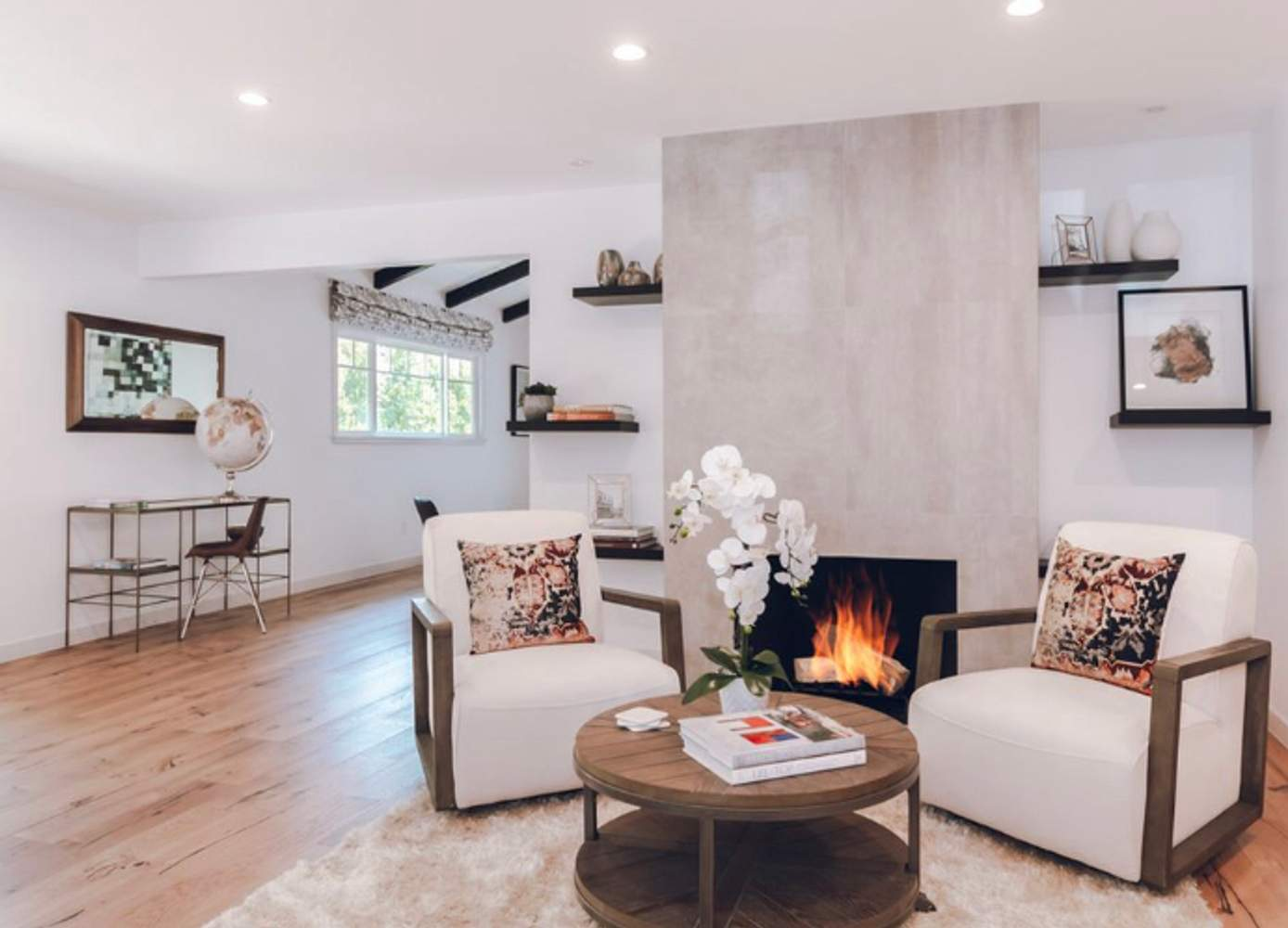 A modern living room featuring two white armchairs, a round wooden coffee table, a fireplace, decorative shelves, and a desk with a globe, showcasing the interior design by Smith & Son Construction in Martinez.
