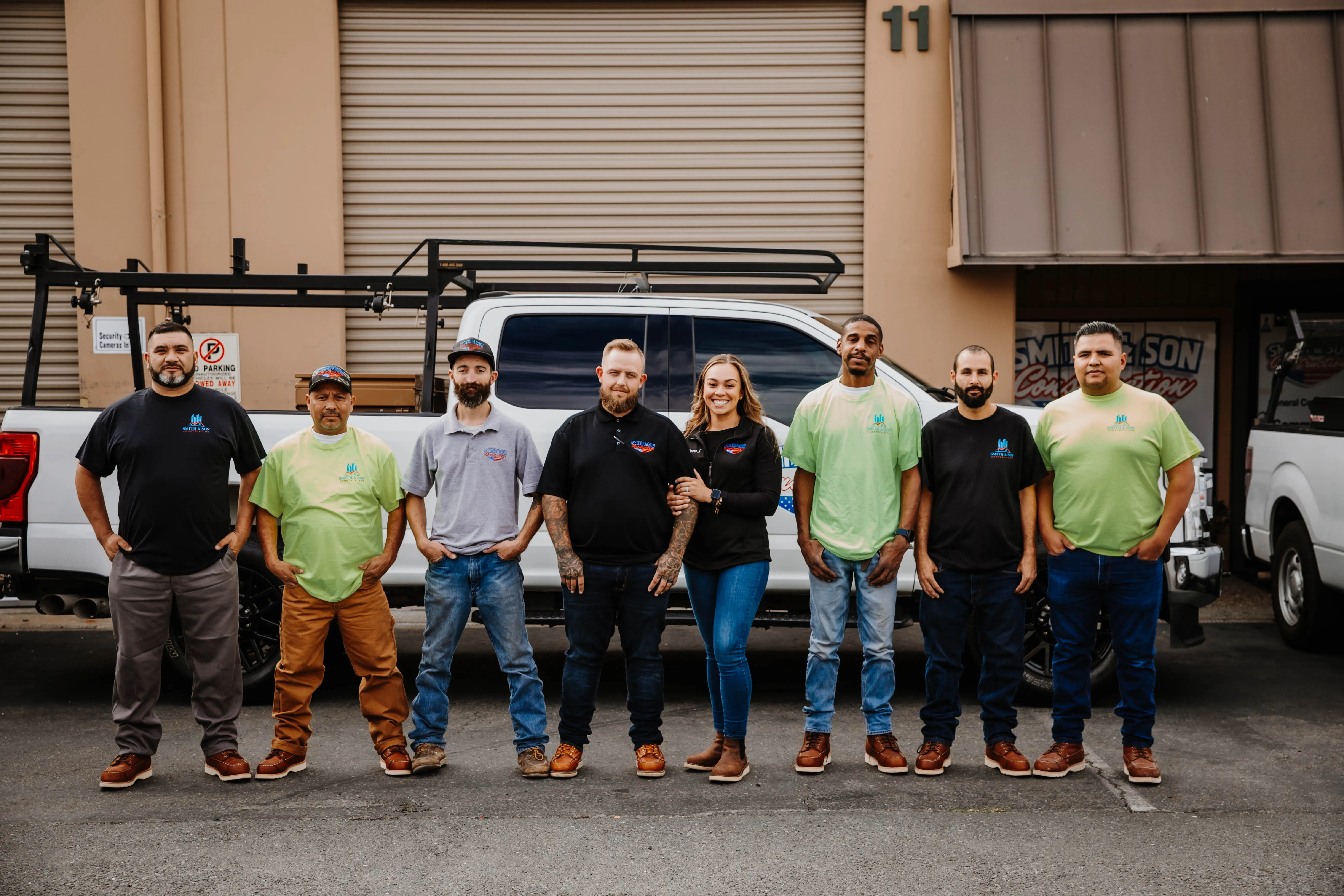 A group of eight individuals from Smith & Son Construction stand together in front of a white truck, displaying their team spirit and readiness to work, with the Smith & Son Construction sign partially visible in Martinez.