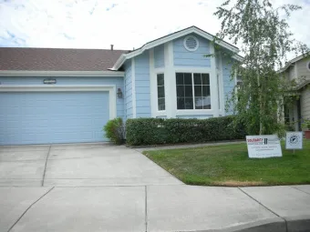 A light blue house with a well-maintained lawn and a sign for Solidarity Painting, Inc. in Santa Rosa displayed on the front yard.