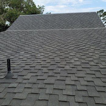 A newly installed shingle roof by South Creek Roofing & Waterproofing Inc., showcasing precise workmanship and uniformity, with trees visible in the background against a blue sky.