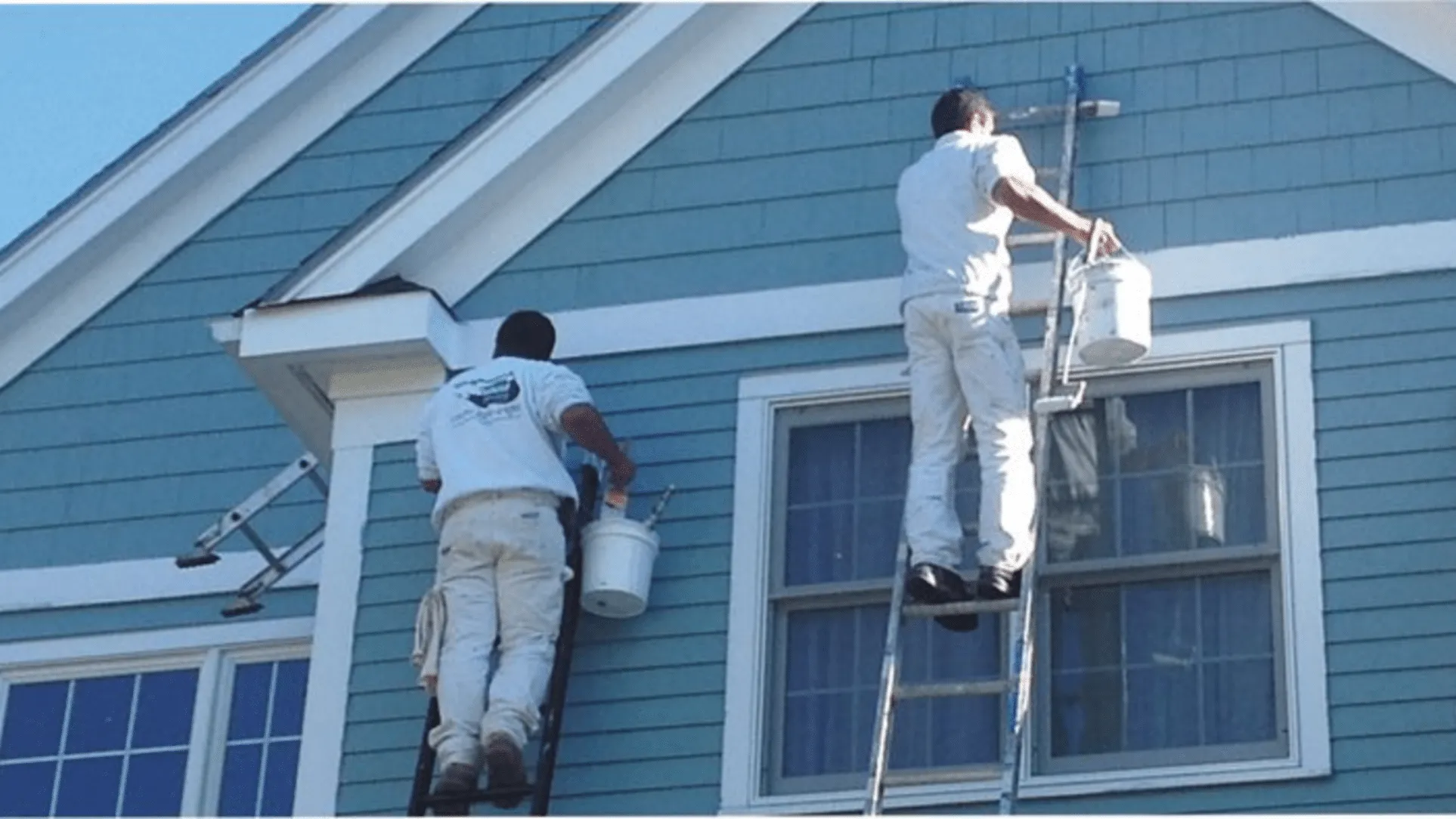 Two painters from Stanford Painting, Inc. working on a blue house in Mountain View, using ladders and paint buckets.