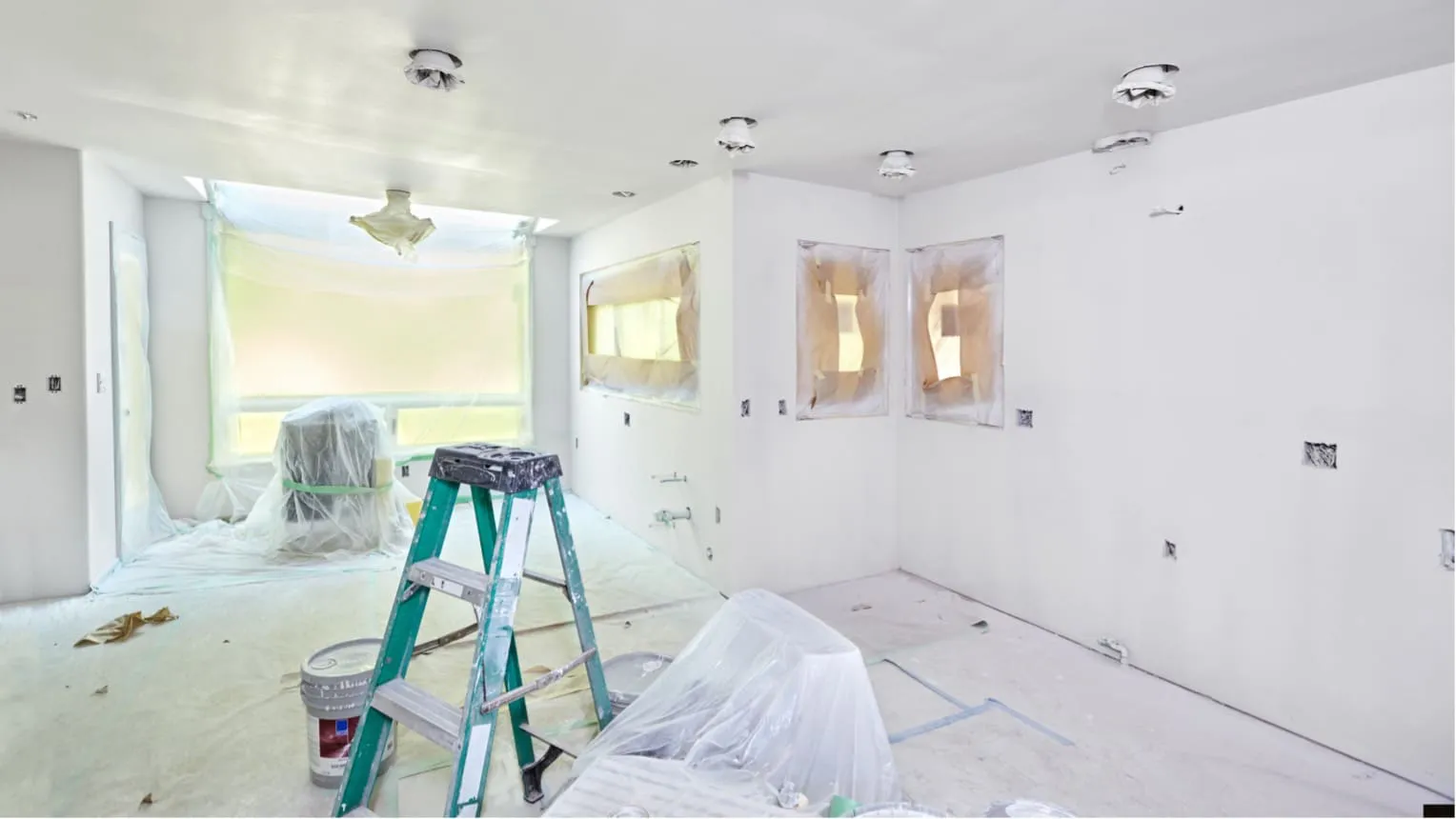 A room under renovation with white walls and protective coverings, featuring a ladder and paint bucket in Mountain View, serviced by Stanford Painting, Inc.