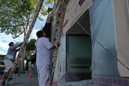 Two painters from Steve Roberts Painting in Walnut Creek are setting up ladders and preparing a building exterior for painting, with protective coverings in place.