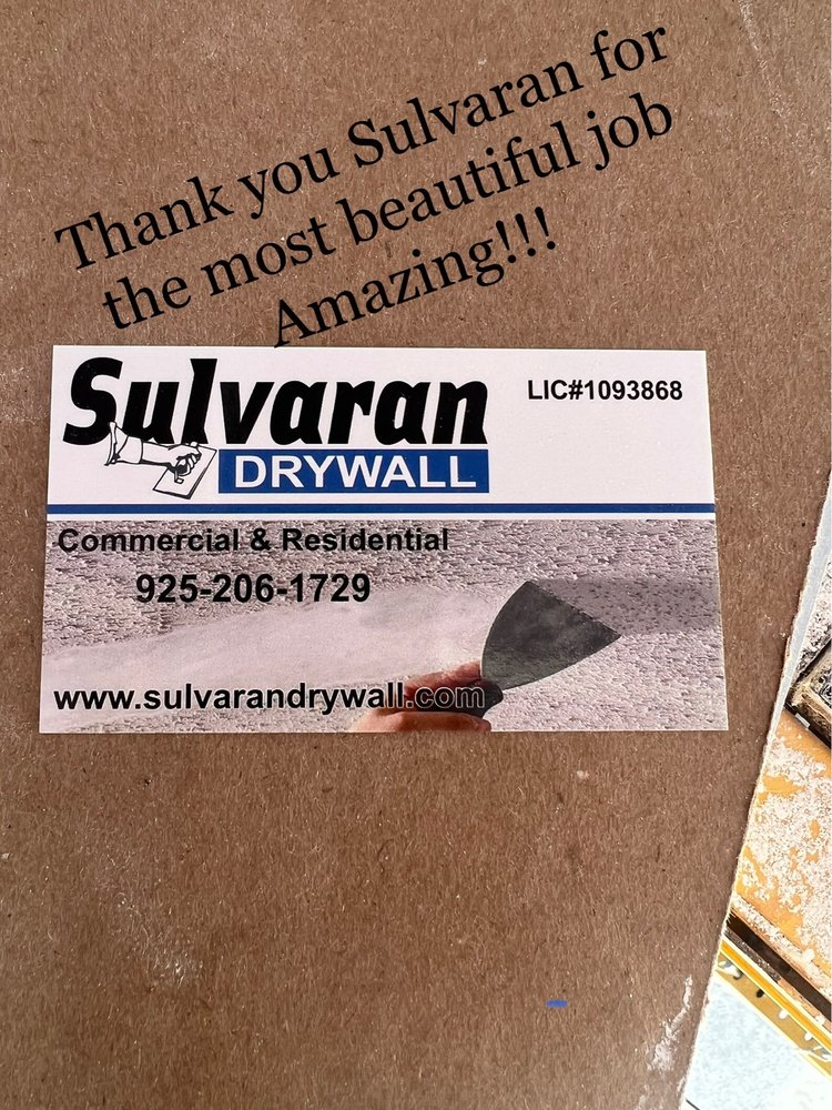 Business card of Sulvaran Drywall with contact details, placed on a brown surface, with a thank you message for their work.