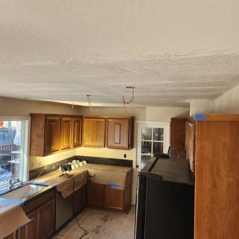 A kitchen under renovation with freshly installed drywall on the ceiling, wooden cabinetry, and covered countertops, completed by Sulvaran Drywall in Antioch.
