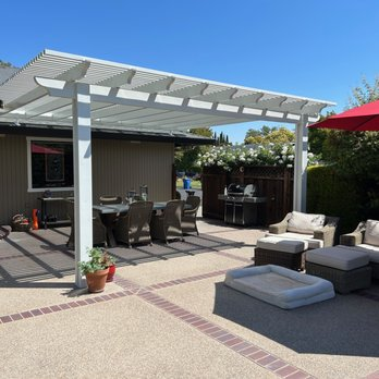 Outdoor patio with a modern white pergola, wicker dining set, and comfortable lounge seating under a clear sky.