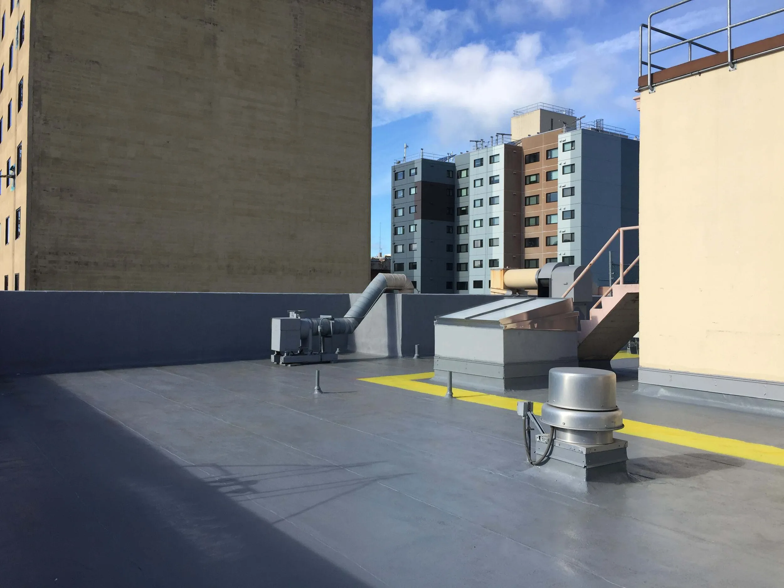A flat rooftop in San Francisco with modern ventilation systems, showcasing the work of Sure Roofing & Waterproofing against a backdrop of urban buildings.