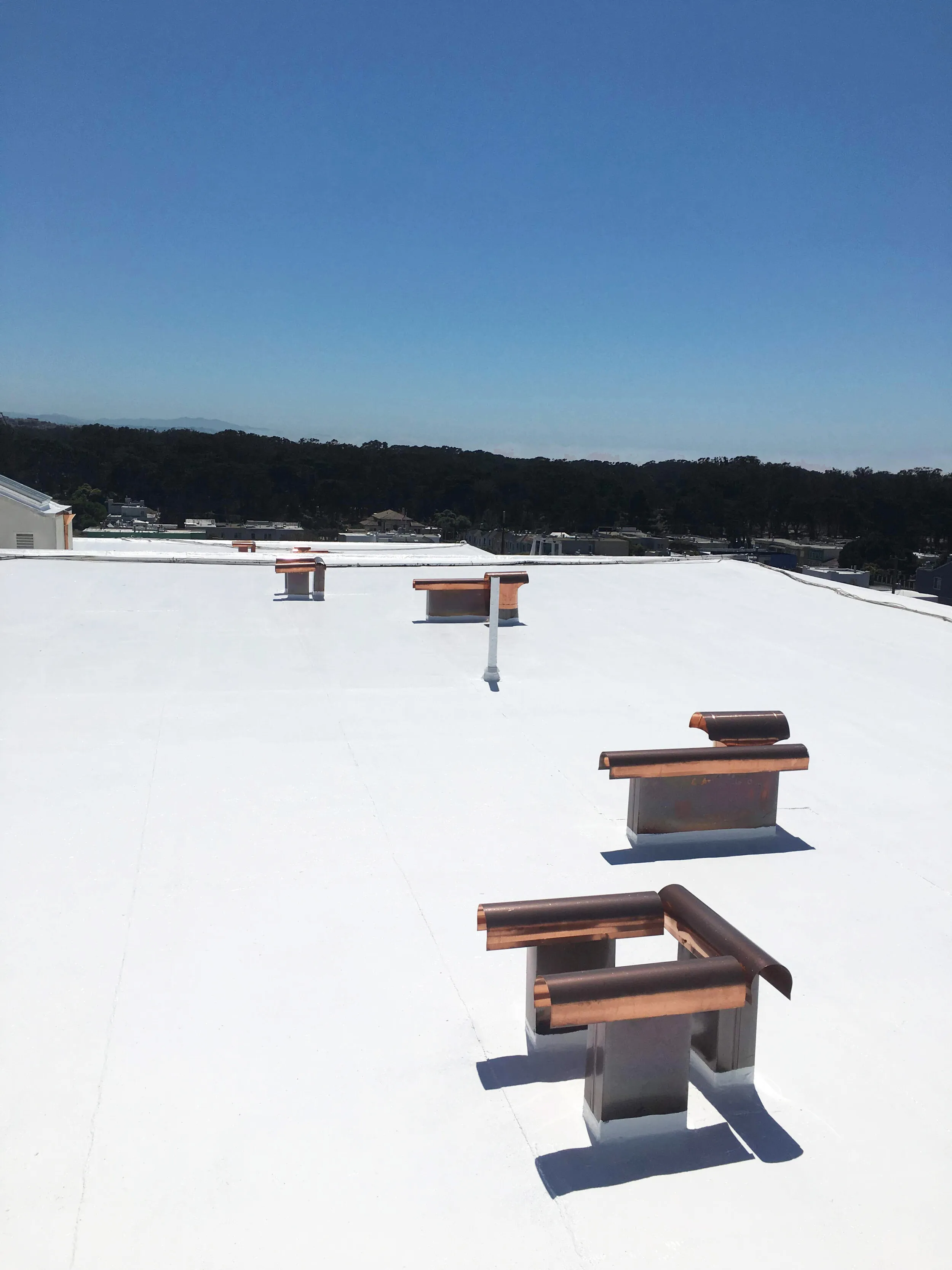 A white rooftop with copper fixtures under a clear blue sky, installed by Sure Roofing & Waterproofing in San Francisco.