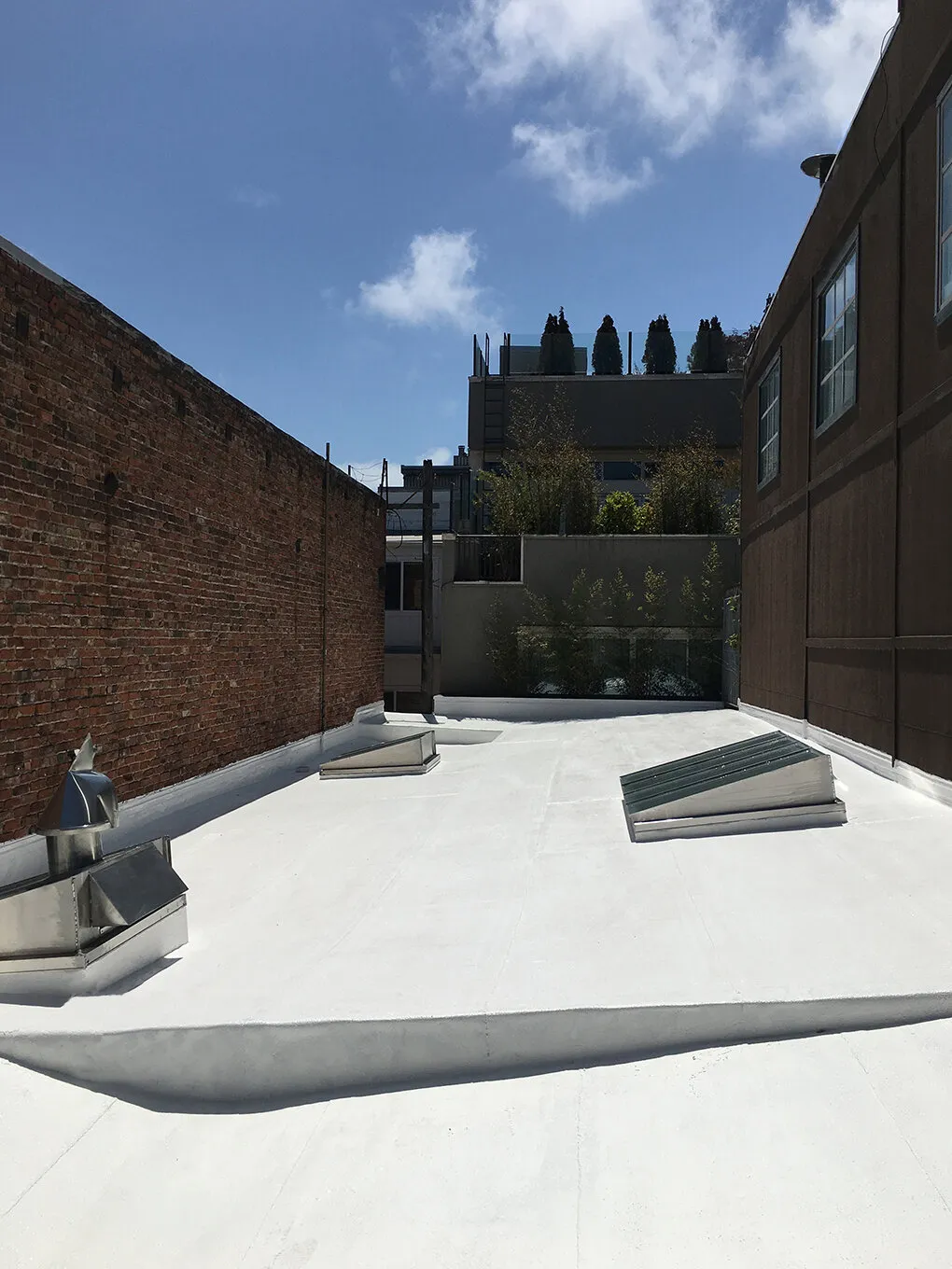 A flat, white rooftop with metal fixtures and skylights, completed by Sure Roofing & Waterproofing in San Francisco, under a blue sky with scattered clouds.