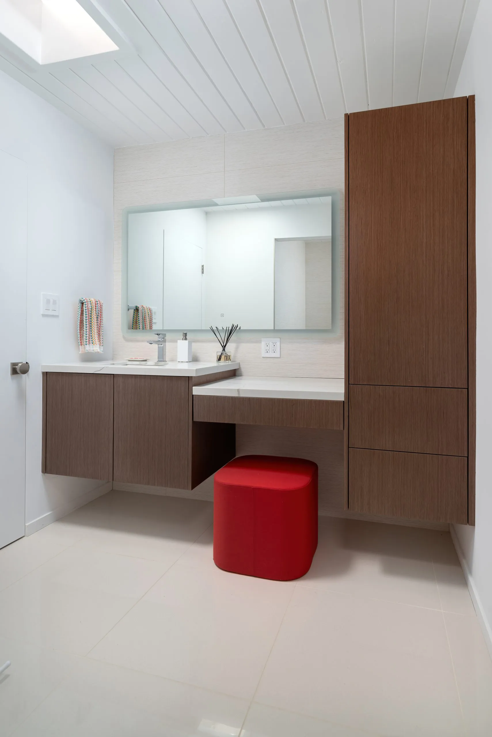 A modern bathroom in Walnut Creek featuring wooden cabinets and a red ottoman, designed by TOP REMODELING & DESIGN.