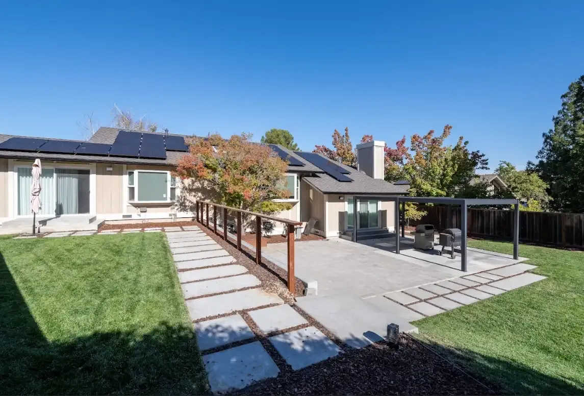 A modern backyard in Walnut Creek featuring solar panels on the roof, a patio with pavers, a pergola, and a landscaped lawn, designed by TOP REMODELING & DESIGN.