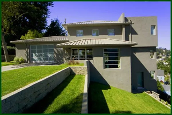 A modern grey house with clean lines and large windows on a grassy hillside, painted by Tara Pro Painting, Inc. in San Francisco.