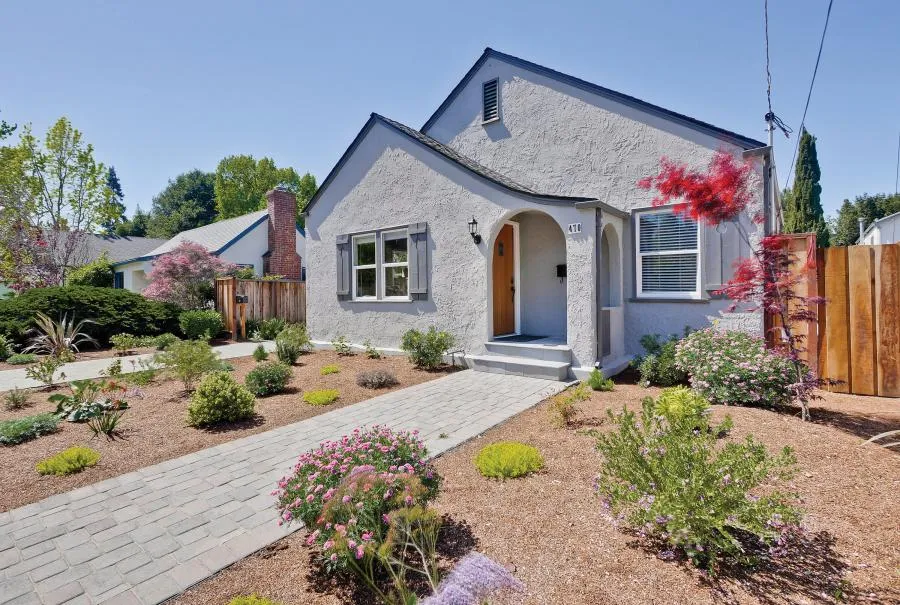 A well-maintained single-story house with a stucco exterior, surrounded by a landscaped garden, under a clear sky in Campbell.