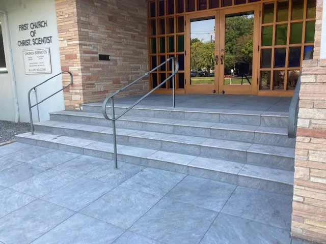 Stone-tiled steps leading to the entrance of a building, featuring metal railings and a beautifully designed wooden door, completed by The Legacy Paver Group in Santa Rosa.