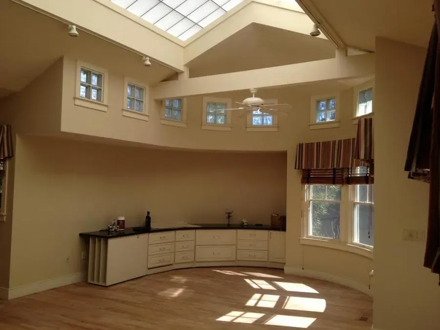 A spacious room with an arched ceiling featuring skylights and small windows, enhanced by a neutral color palette and elegant cabinetry.