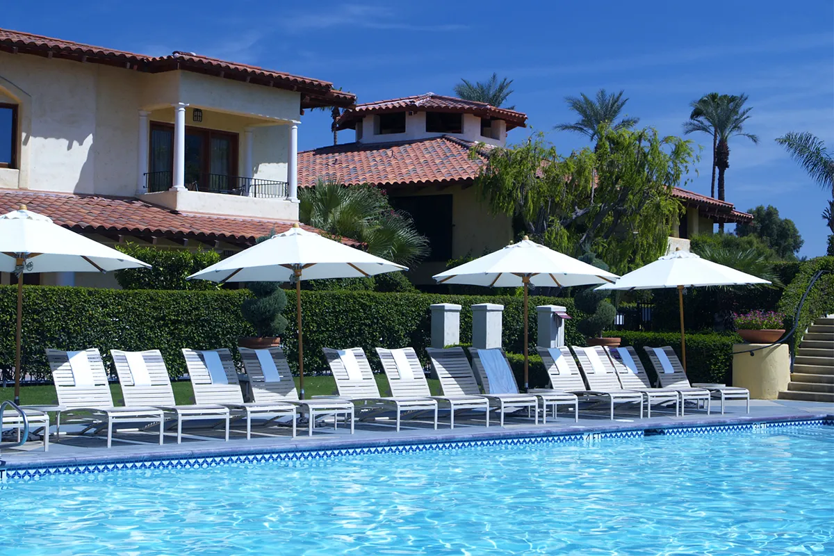 View of a luxurious swimming pool surrounded by lounge chairs and umbrellas, with a villa in the background.