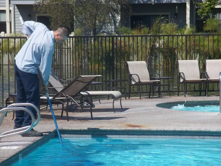 A professional pool cleaner from The Pool Doctor in El Sobrante carefully maintaining a swimming pool using a skimmer net.