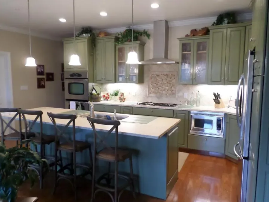 A modern kitchen in Healdsburg featuring green cabinetry, a large island with chairs, pendant lighting, and stainless steel appliances by Thompson Construction, Inc.