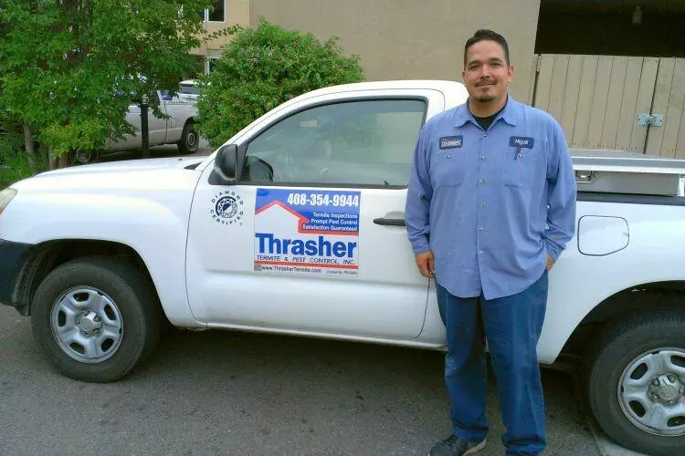 A person in a blue uniform standing next to a white truck with Thrasher Termite & Pest Control, Inc. logo in Los Gatos.