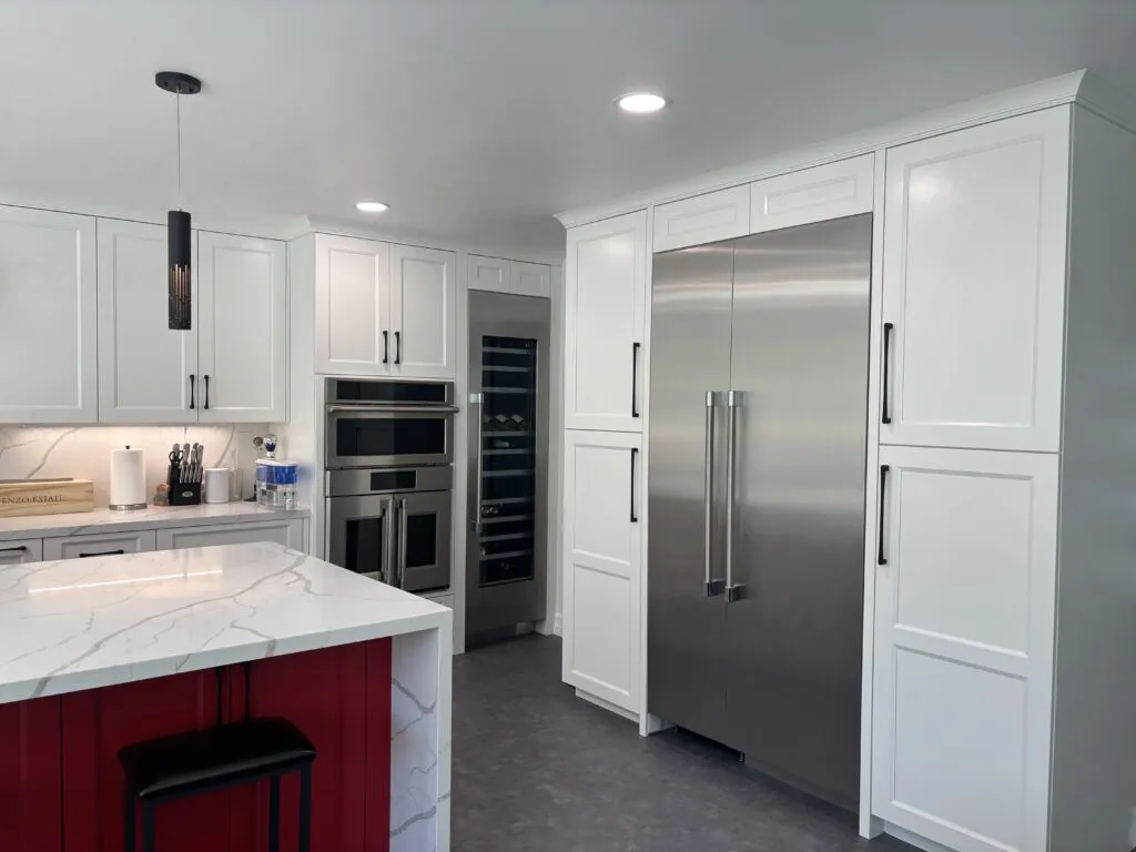 A modern kitchen featuring white cabinetry, a large stainless steel refrigerator, and a red island with a marble countertop, designed by Today'sKitchen&Bath in Livermore.
