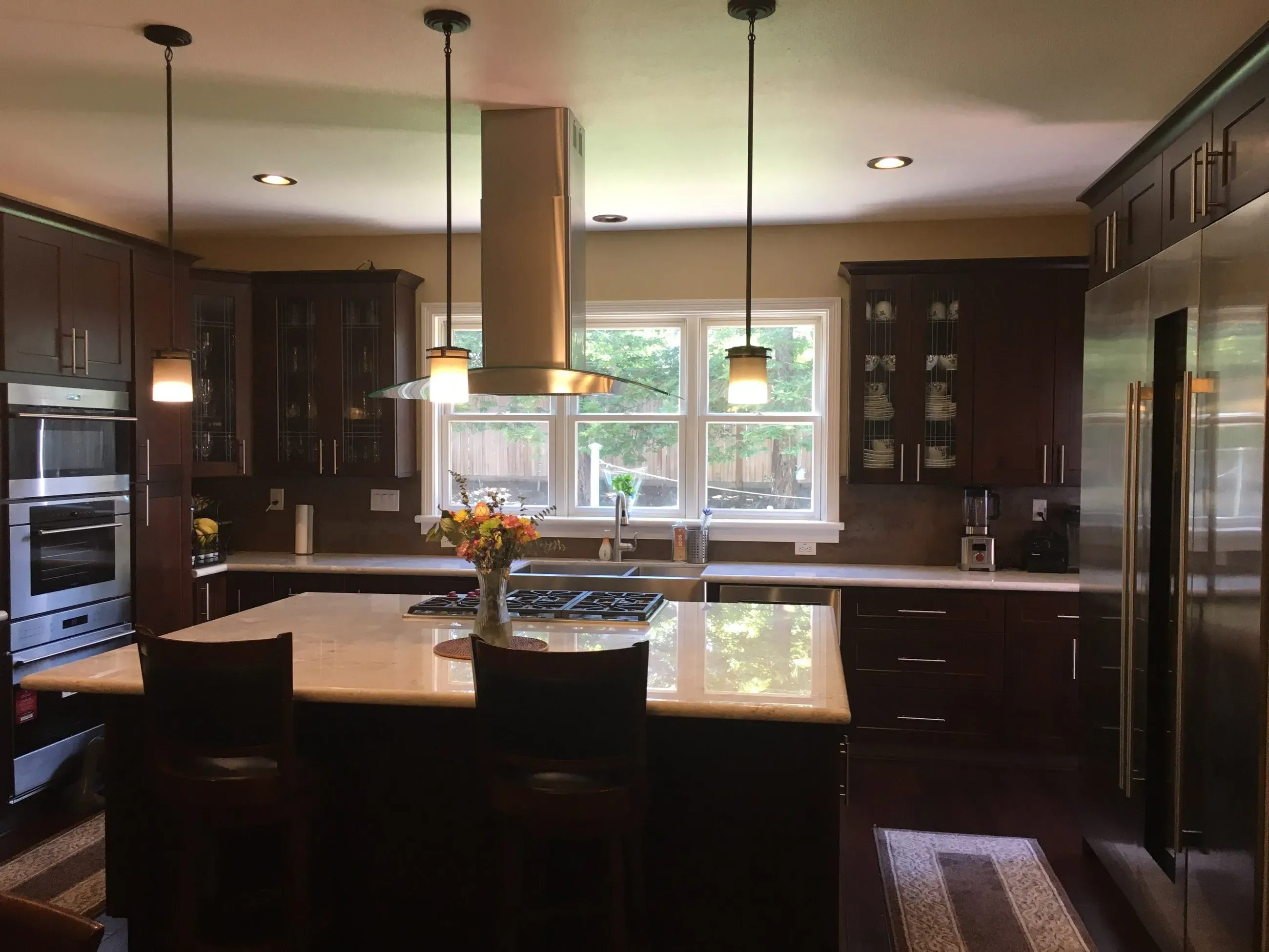 Modern kitchen interior with dark wood cabinets, stainless steel appliances, and a central island, featuring a vase of flowers, by Today'sKitchen&Bath in Livermore.