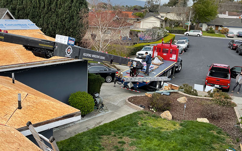 A roofing crew from Top Tier Roofing working on a roof installation using a crane to lift materials in a residential neighborhood in Morgan Hill.