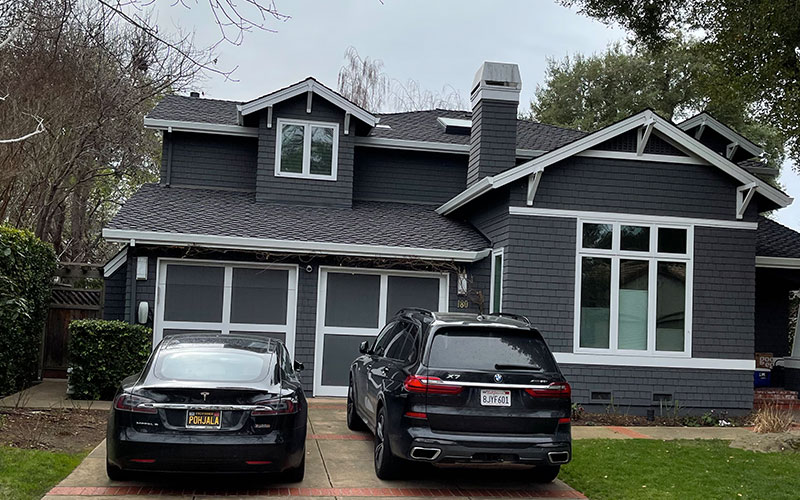 A modern black-roofed gray house in Morgan Hill with two cars parked in the driveway, showcasing a renovation by Top Tier Roofing.