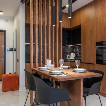 A modern kitchen and dining area designed by True Builders in San Jose, featuring wood cabinetry, a dining table with black chairs, and minimalist pendant lighting.