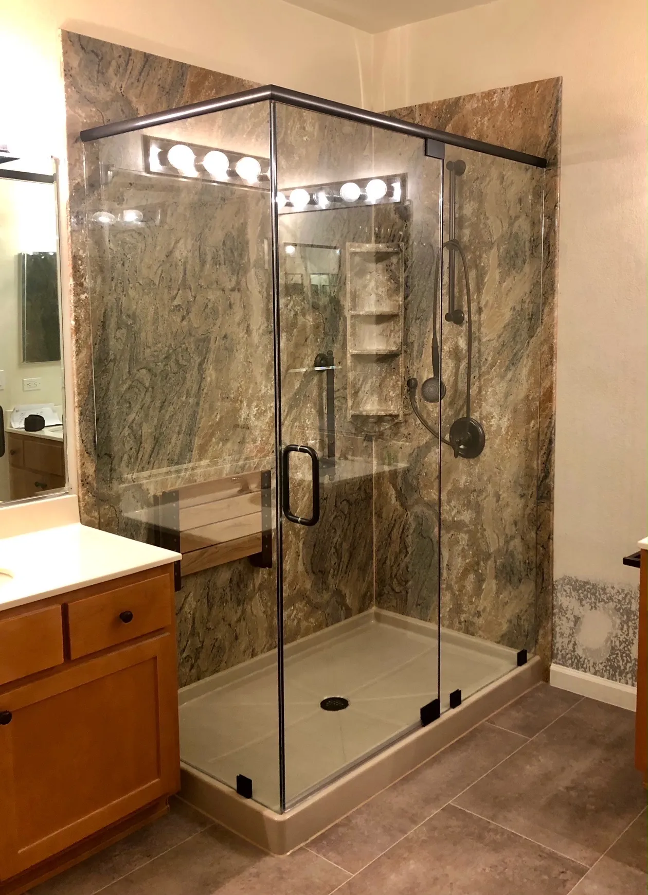 A modern glass shower enclosure with stone tile walls and a built-in bench, part of a bathroom by TrueNorthKitchen&Bath in San Mateo.