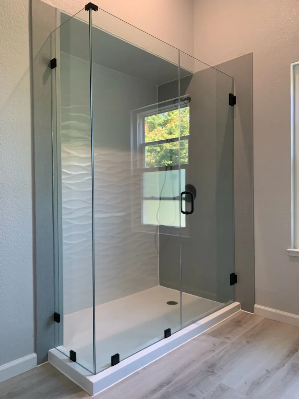 A modern glass shower enclosure with wave-textured white tiles and a sleek design, installed by TrueNorthKitchen&Bath in San Mateo.