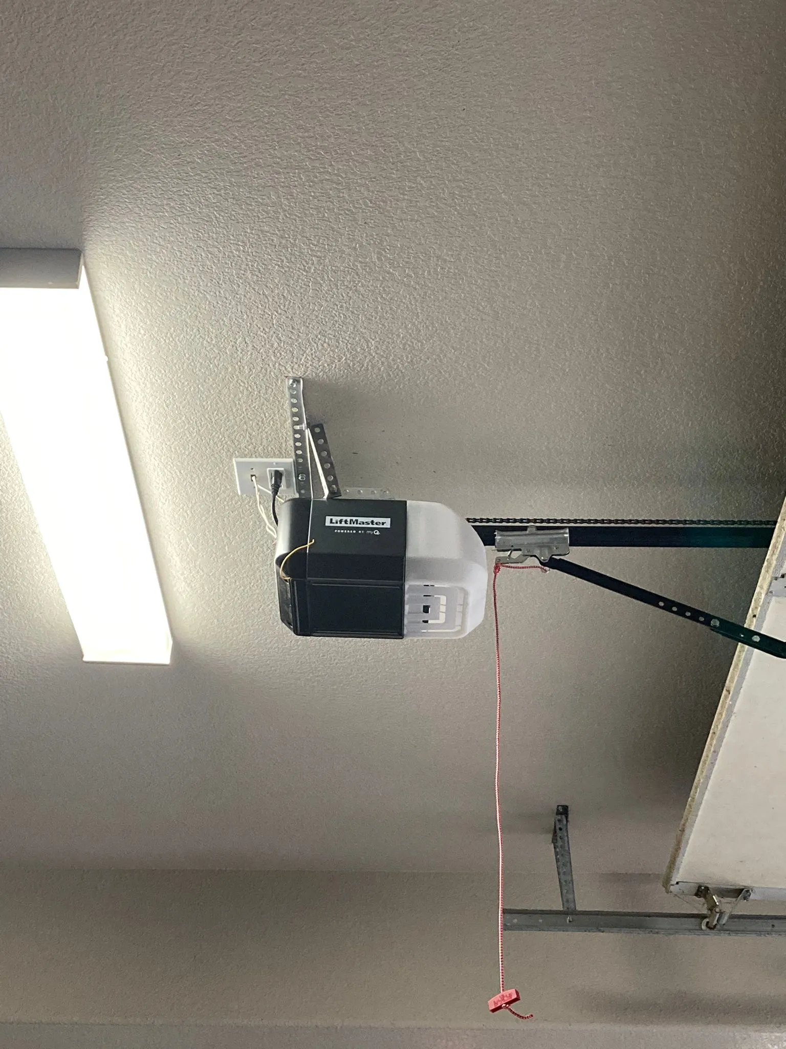 Image of a ceiling-mounted garage door opener with a hanging red pull cord in a garage, installed by Turbo Garage Door in Santa Rosa.