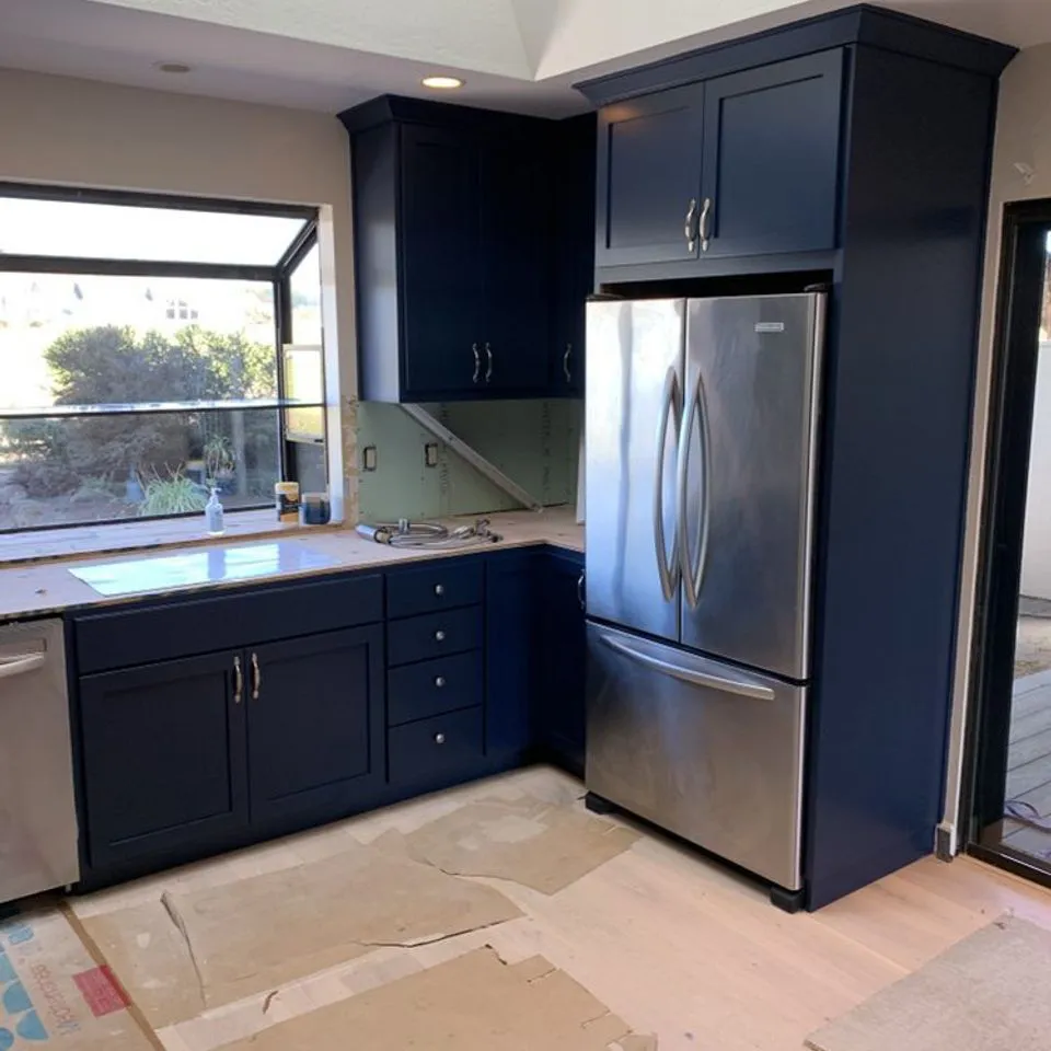 A kitchen with newly painted deep blue cabinets, a stainless steel refrigerator, and a window overlooking greenery, showcasing Unique Painting Services' work in Novato.