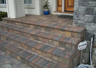 Stone steps and landing with varying shades of earth-toned pavers leading to a wooden door, designed by Unique Pavers in San Jose.