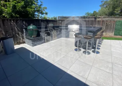 Outdoor patio in San Jose featuring large tile flooring, a modern grill, and bar seating, designed by Unique Pavers.