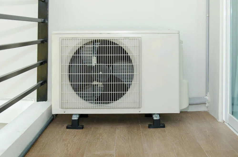 Exterior view of an air conditioning unit installed on a wooden floor, next to a wall and railing, used for indoor climate control.