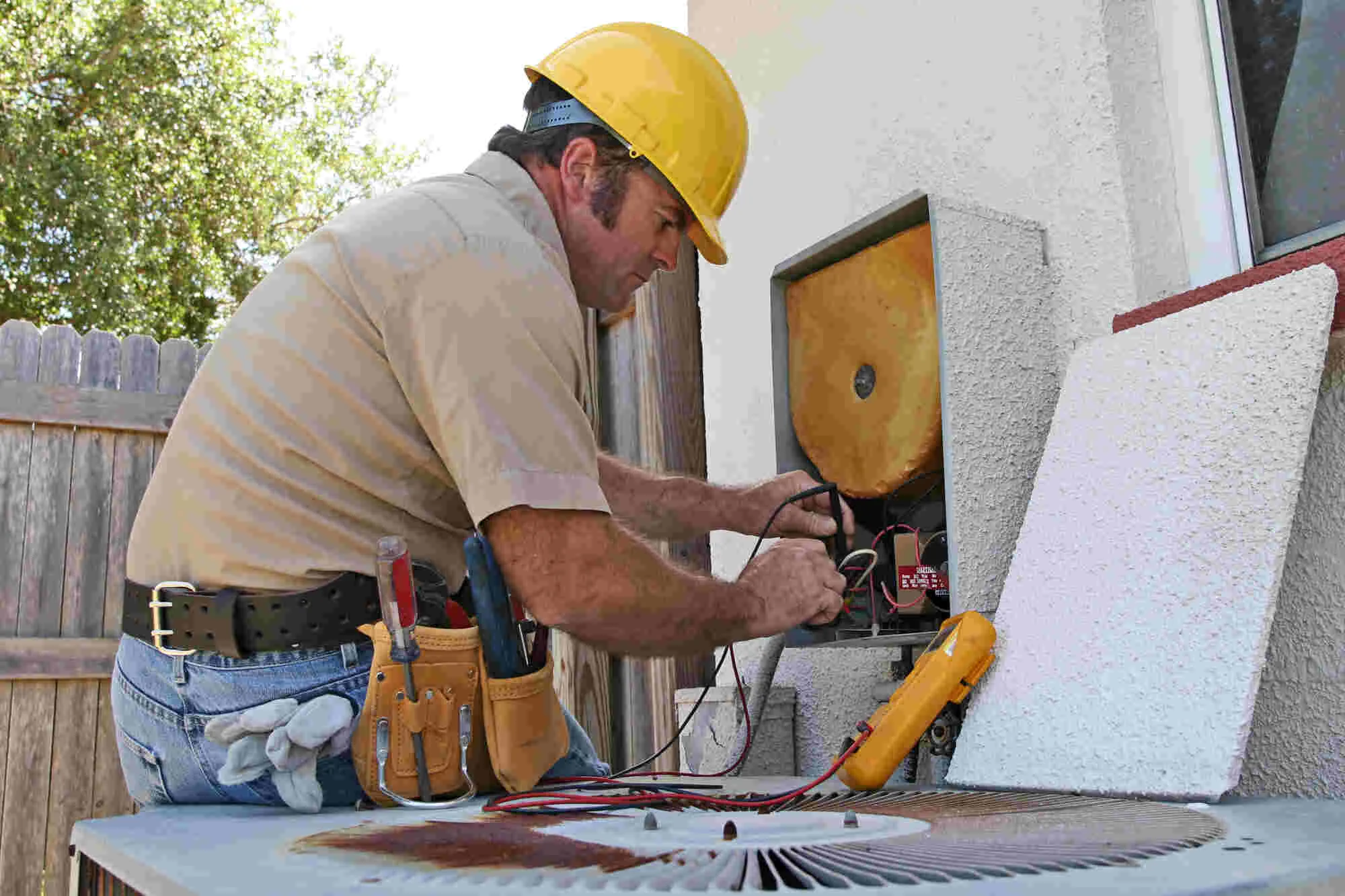 "A technician from Valley Comfort Heating and Air in Santa Rosa working on an outdoor air conditioning unit, wearing a yellow hard hat and using tools to make adjustments."