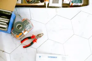A set of pliers, tape, and a box of building supplies are on a hexagonal tile floor, representing the tools used by We Love Small Jobs Handyman Services-Remodelers & Builders in Oakland.