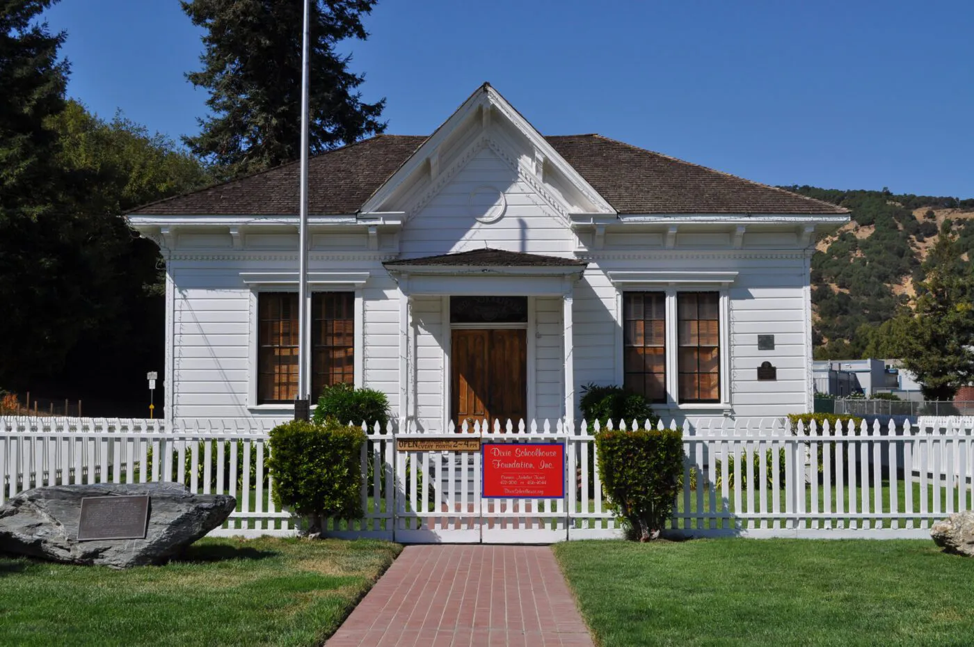 "A beautifully maintained white historic building in Petaluma, featuring a well-kept roof by WedgeRoofing, surrounded by a white picket fence and greenery."