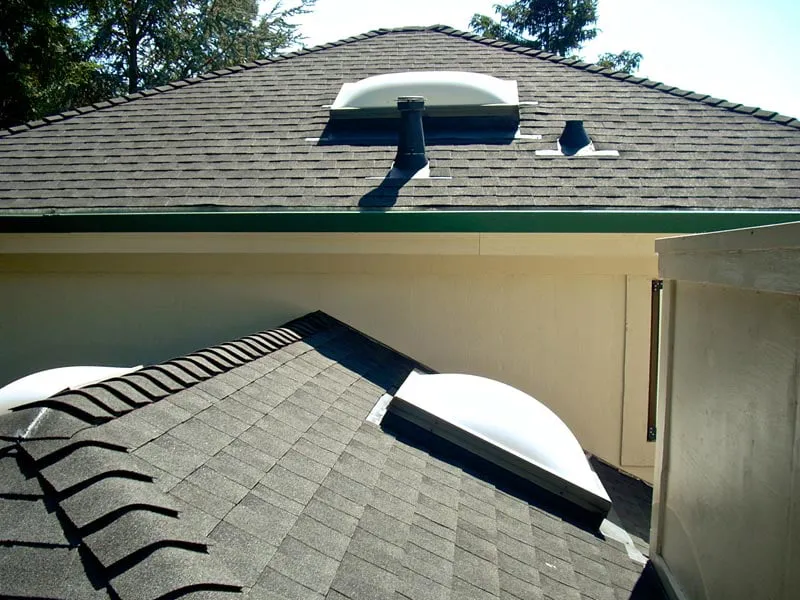 A detailed view of a roof with shingles and two domed skylights, installed by WedgeRoofing in Petaluma.