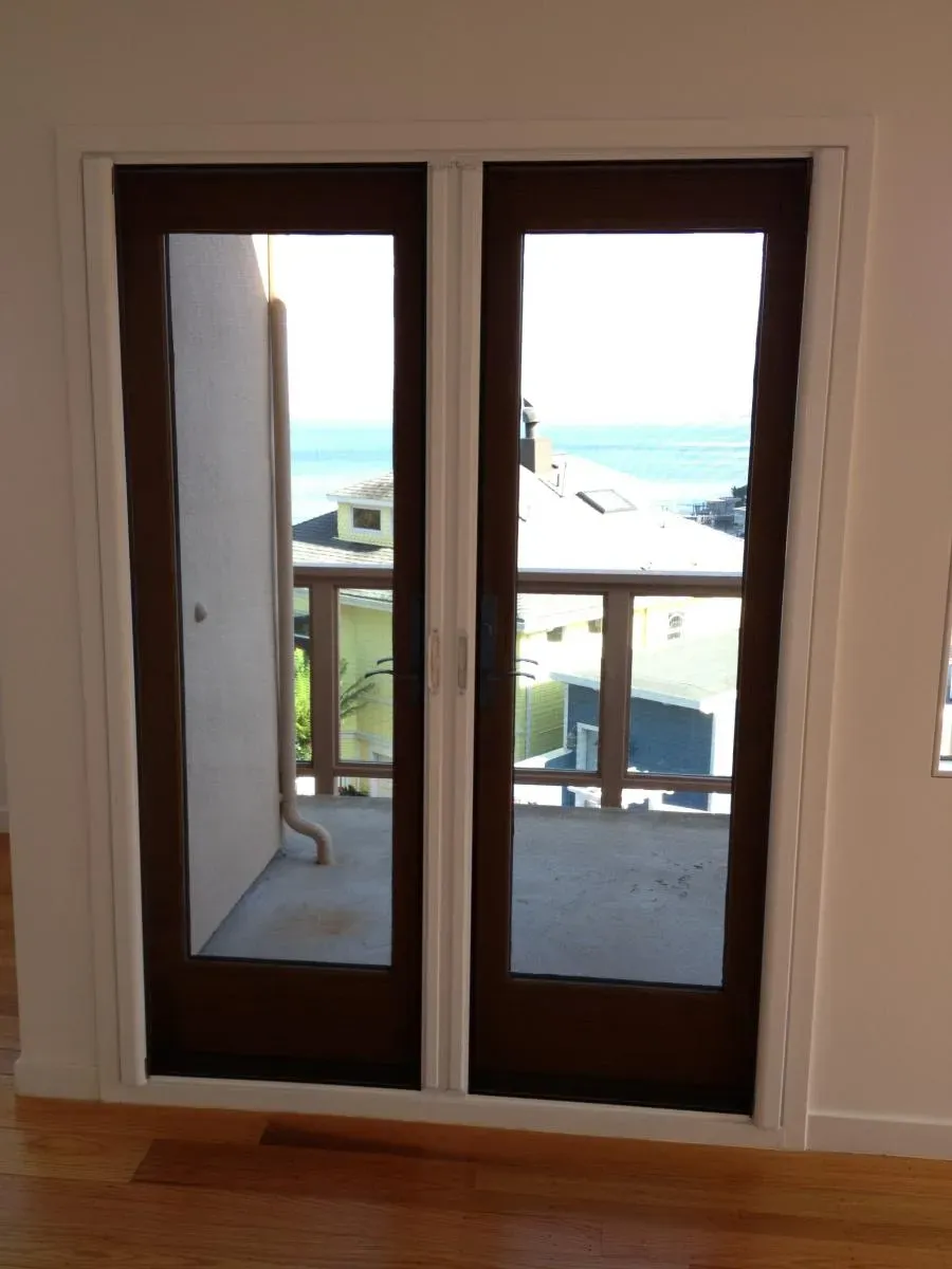 A pair of glass doors leading to a balcony with a view of the ocean, installed by Wesco Screen Company Inc. in San Rafael.