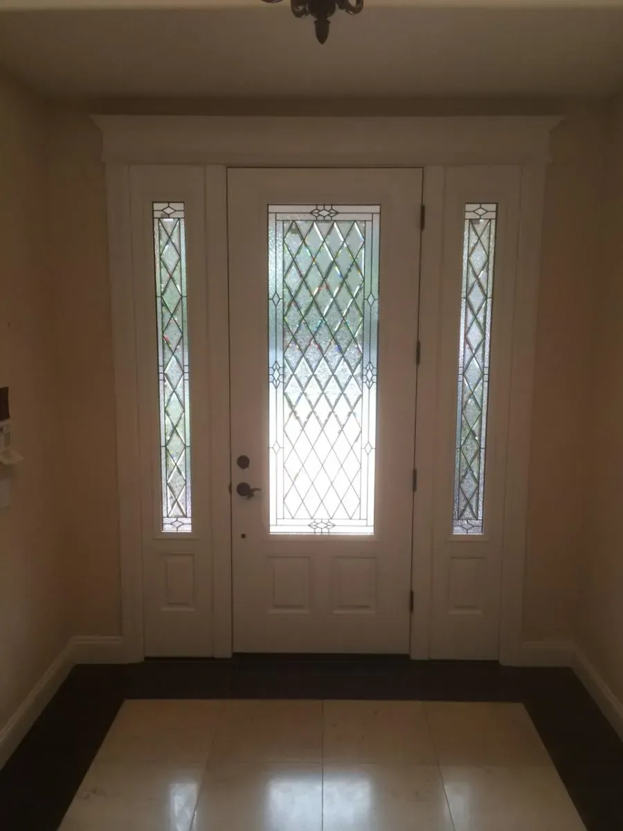 A stained glass front door with side panels featuring geometric patterns, installed in a well-lit interior space.