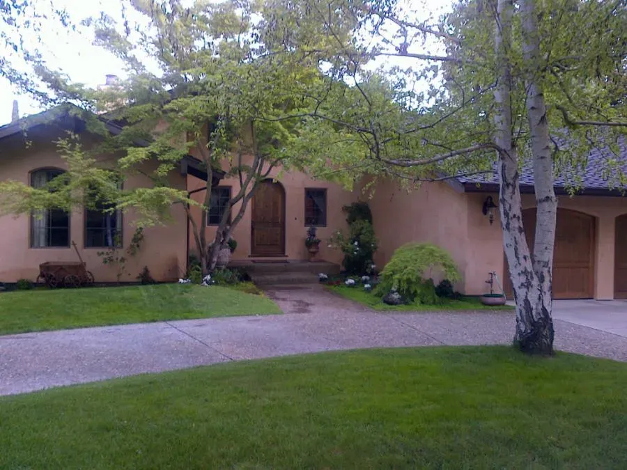 A brown stucco house with wooden doors and windows, surrounded by lush greenery and trees, showcasing the elegant craftsmanship of West Coast Windows and Doors, Inc. in Concord.