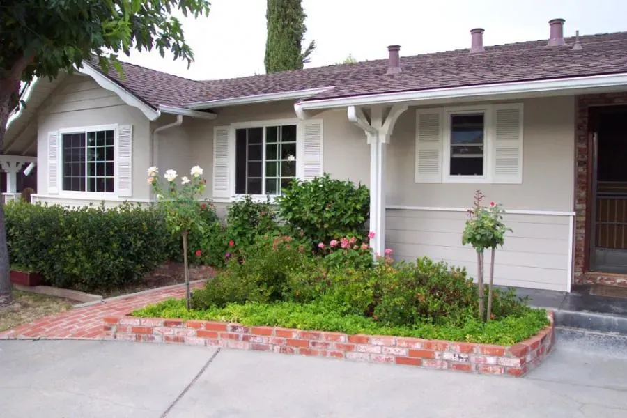 A charming home exterior in Concord with white-framed windows surrounded by lush greenery, featuring installations by West Coast Windows and Doors, Inc.