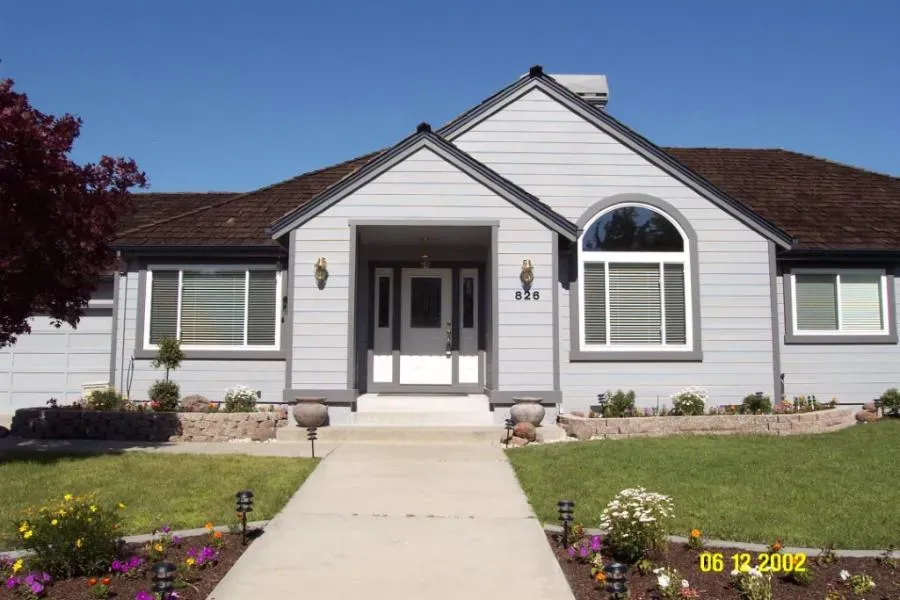 A front view of a single-story house with a manicured lawn and flower beds, featuring elegant windows and doors installed by West Coast Windows and Doors, Inc.