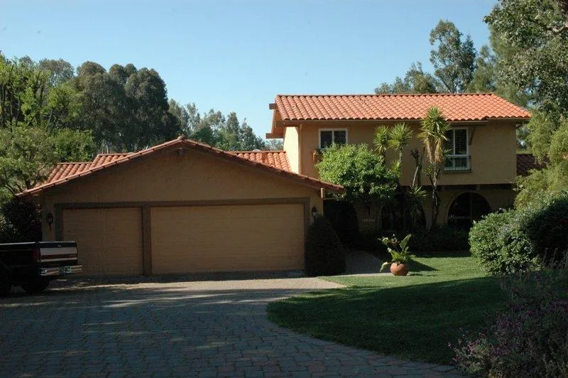 A two-story house with red-tiled roofs surrounded by trees and shrubs, showcasing the roofing work by Westshore Roofing, Inc. in San Jose.