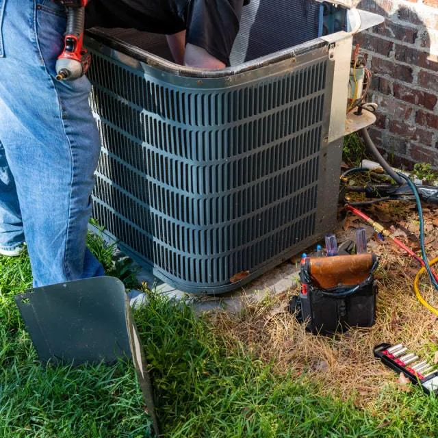 A technician from Wightons Plumbing, Heating, & Air Conditioning in San Luis Obispo is working on an outdoor air conditioning unit with tools around.