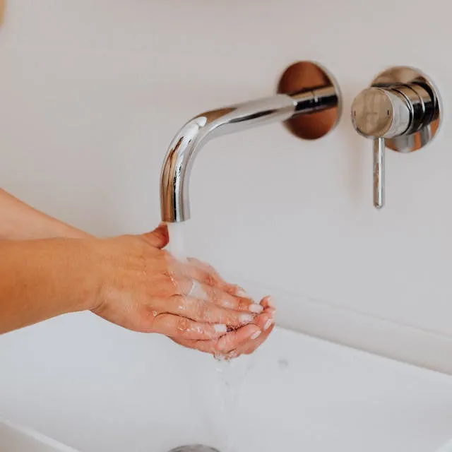 A person washing hands under a modern wall-mounted faucet with water flowing.
